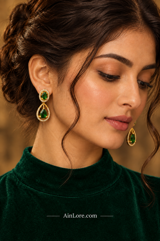 Flatlay of emerald teardrop earrings on burgundy velvet